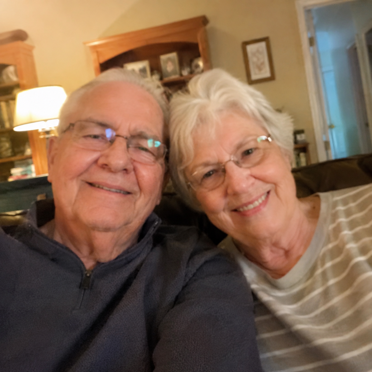 Elderly couple smiling in their living room, slightly shaky cell phone style photo.