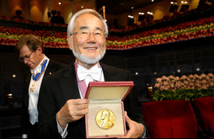 Dr. Yoshinori Ohsumi on stage receiving an award, with his wife Mariko beside him